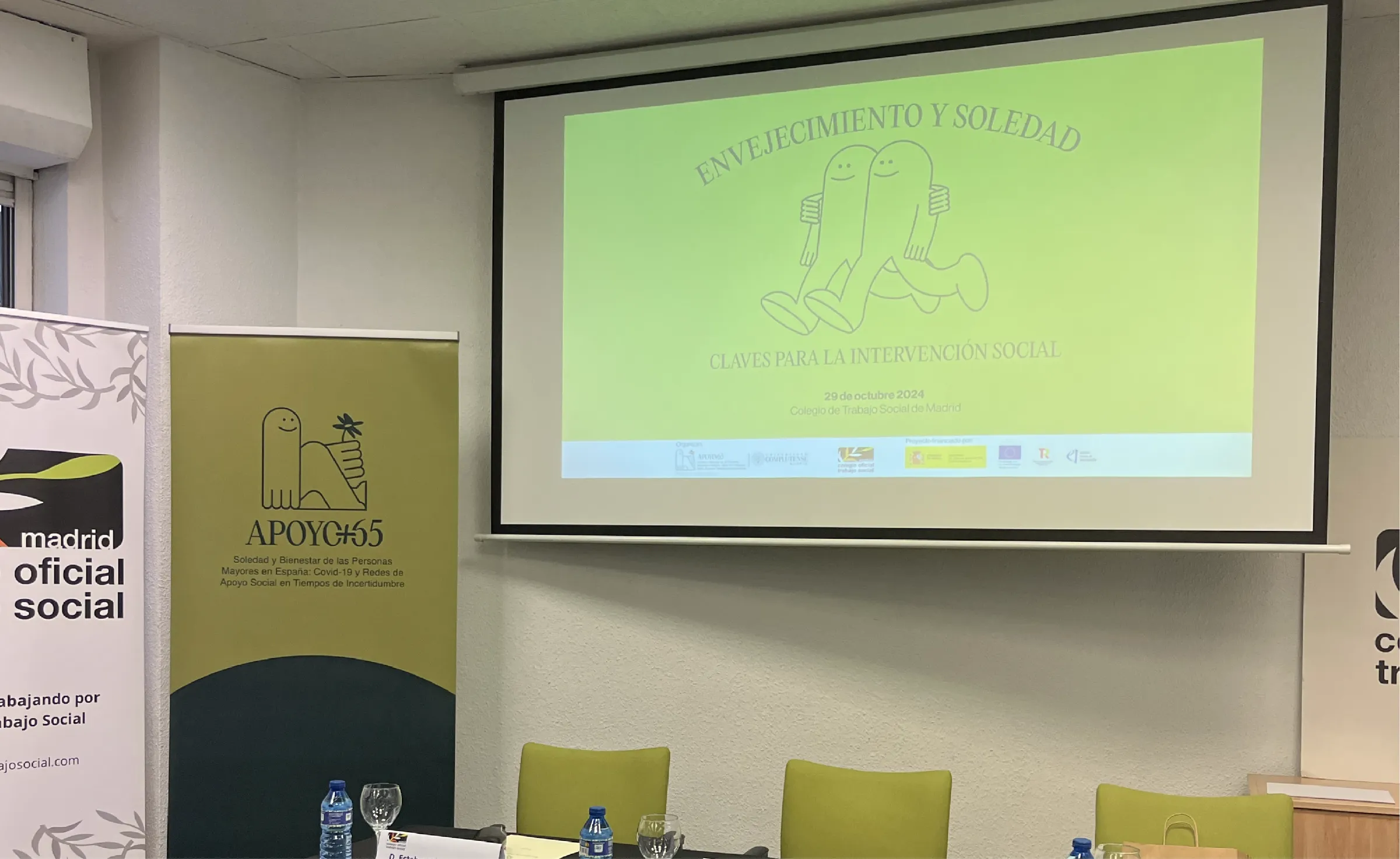 Sala de conferencias con el roll-up de APOYO+65 y los gráficos del evento en la pantalla
